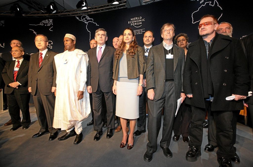 “Group of world leaders, philanthropists, and influencers standing together at the World Economic Forum event, with the forum’s logo and world map in the background.”